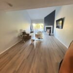 Spacious living room with wooden flooring, a small dog, sofa, TV, and large windows, after professional move-in cleaning